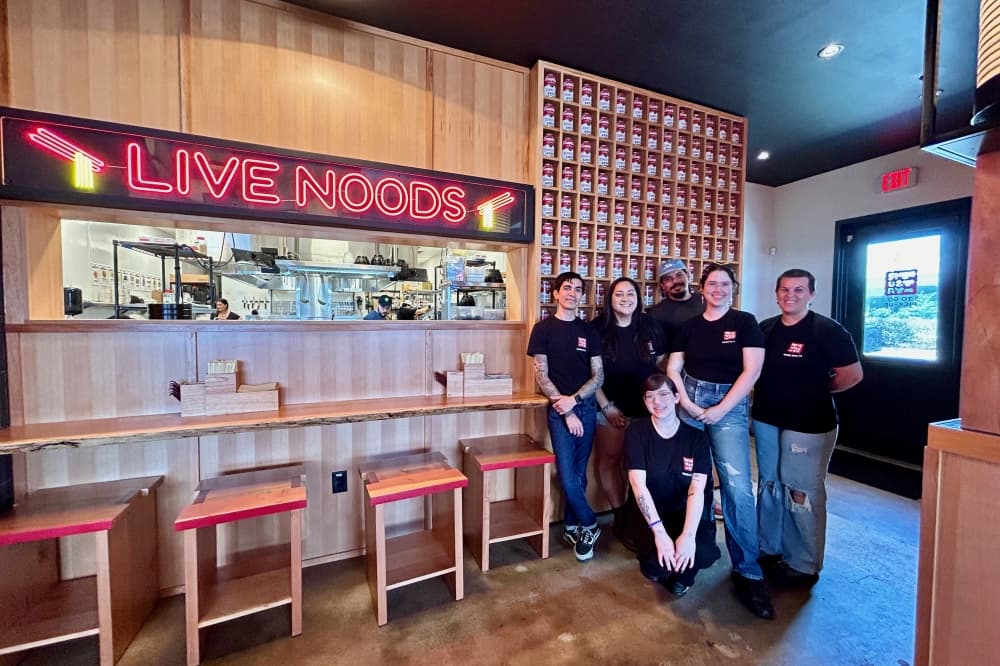 The Ramen Tatsu-Ya Round Rock team stands near custom signage and Campbell's Soup can-style artwork. (Brooke Sjoberg/Community Impact)