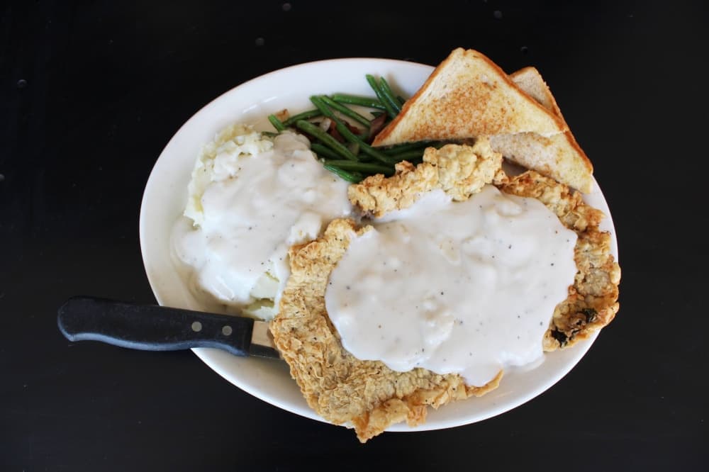Chicken fried steak with gravy potatoes beans and bread.