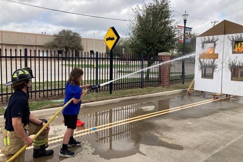 Firefighter helping child with water hose in a fire fighting scenario. 