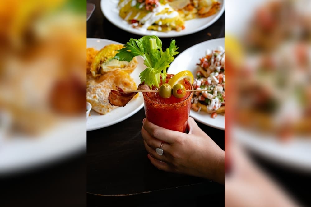 Hand holding a Blood Mary in front of plates