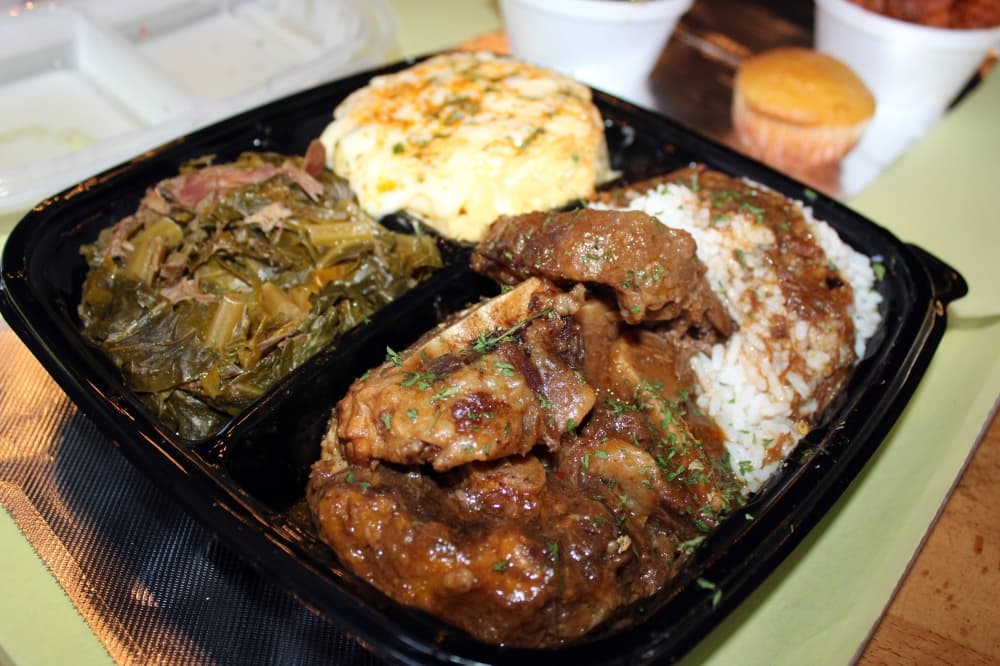 Cooked oxtail with sides of greens, mac and cheese and rice with brown gravy. 