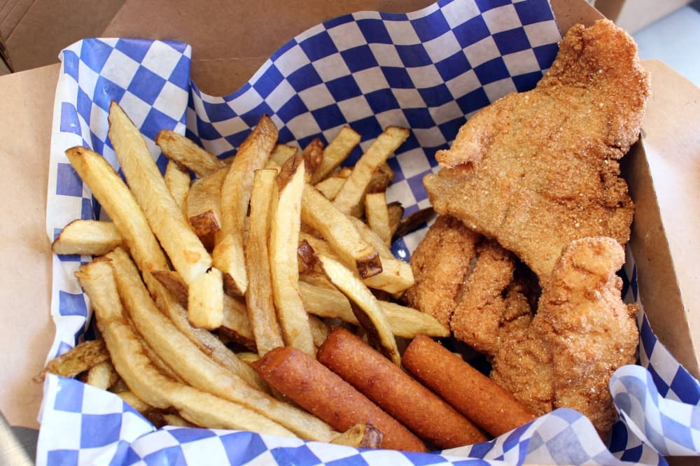 Catfish, french fries, hushpuppies in a a brown box with white and blue checked paper liner. 