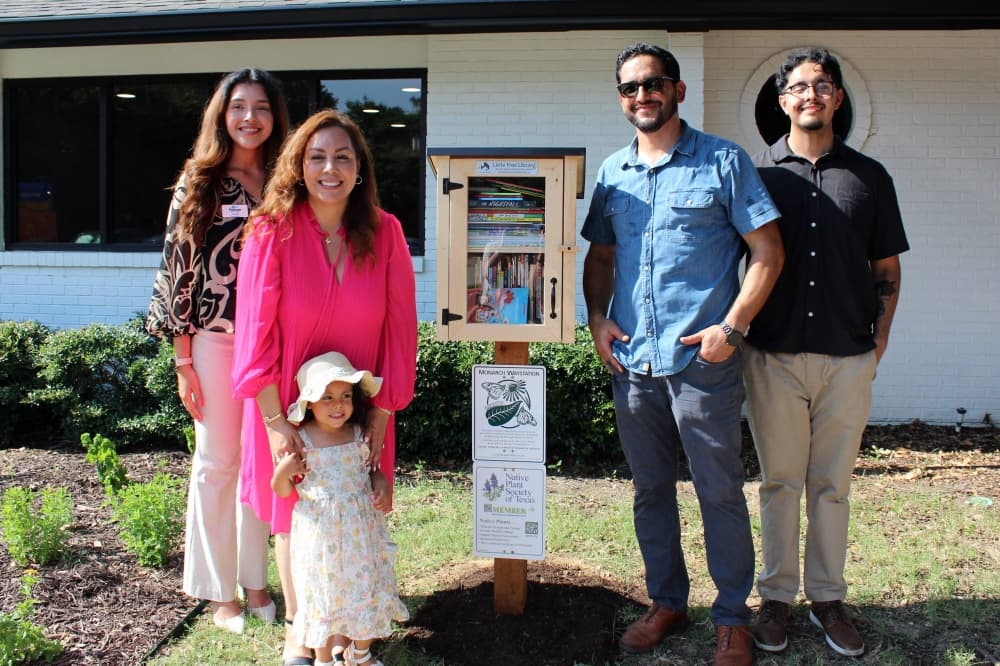 Five people standing next to a little library. 