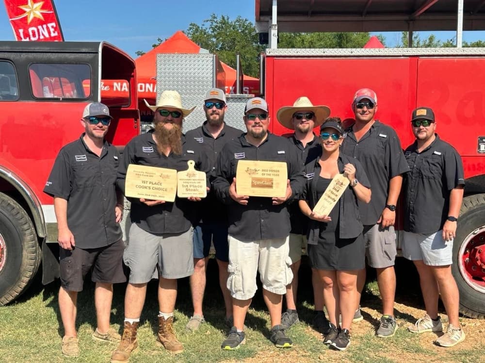 The team holds up awards at a previous barbecue cookoff.