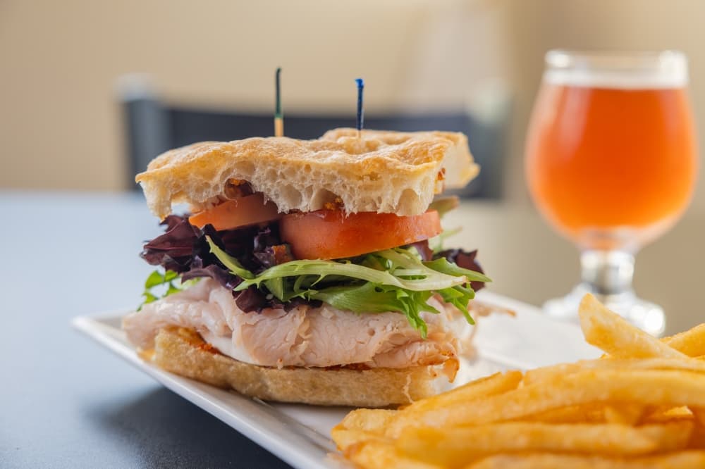 A stacked turkey sandwich with fries and a beer are shown.