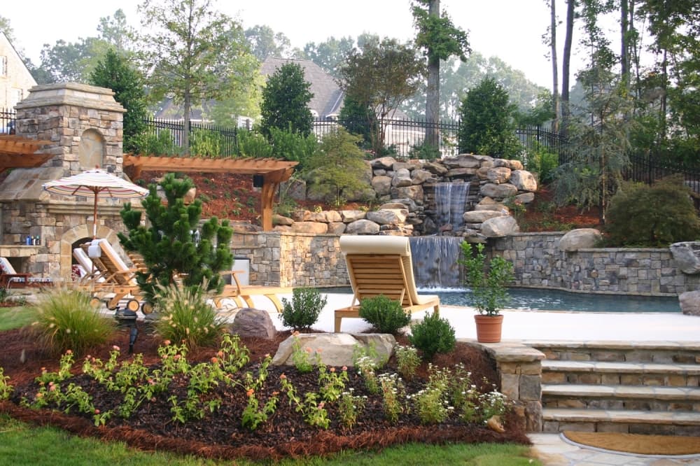 A backyard area with plants, a pool and waterfall is shown.