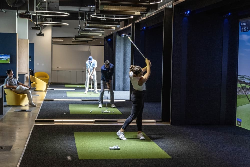 People using golf simulators to play virtual golf courses. 