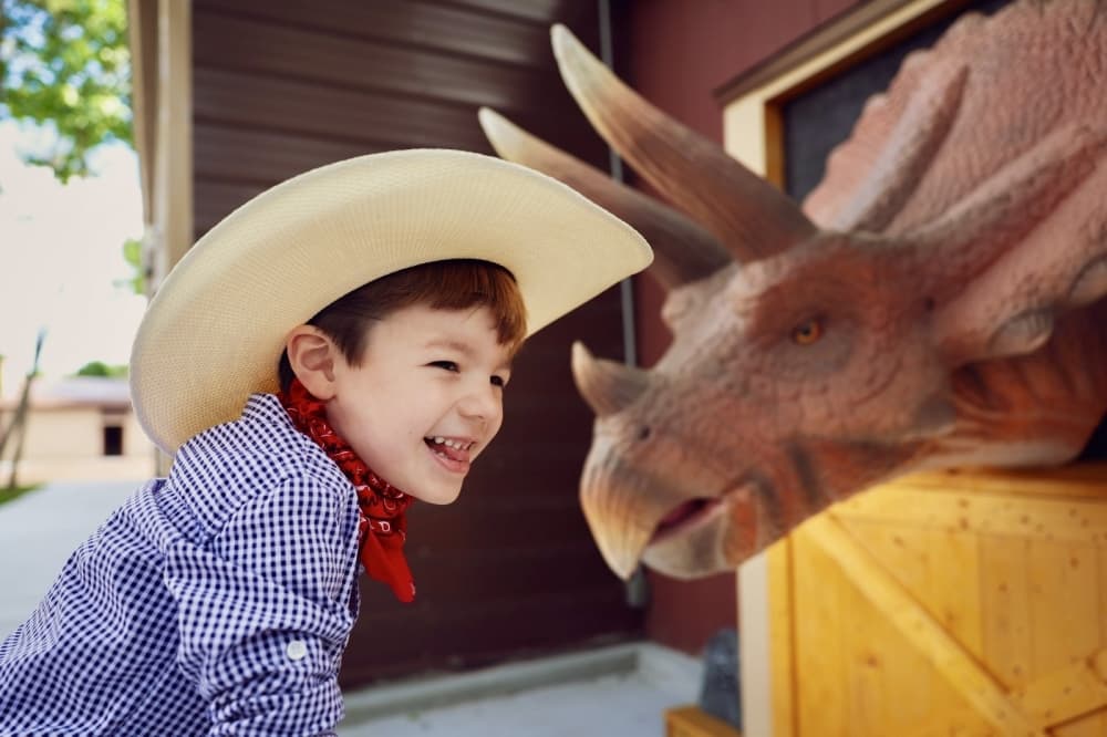Kid in cowboy hat with dinosaur 
