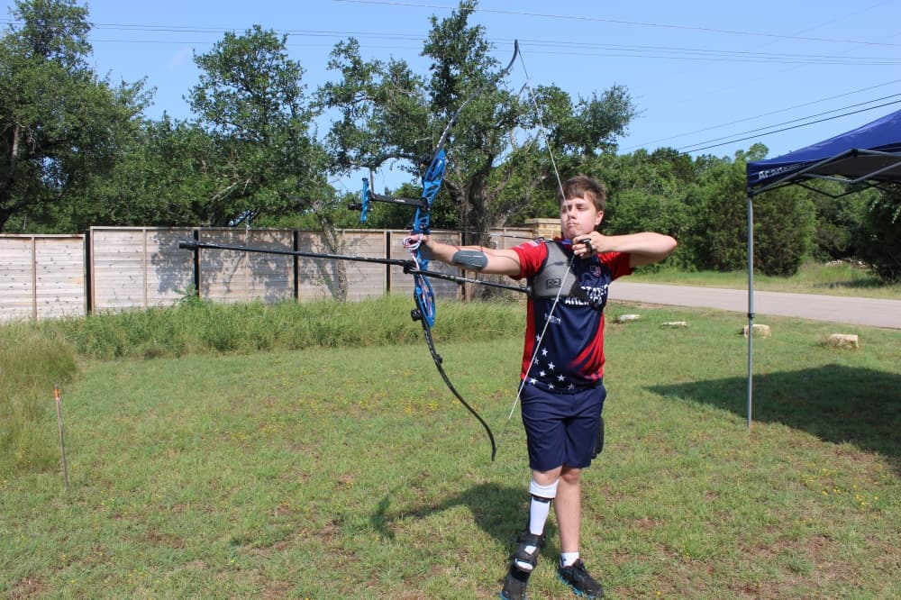 A teenage boy shoots a bow and arrow