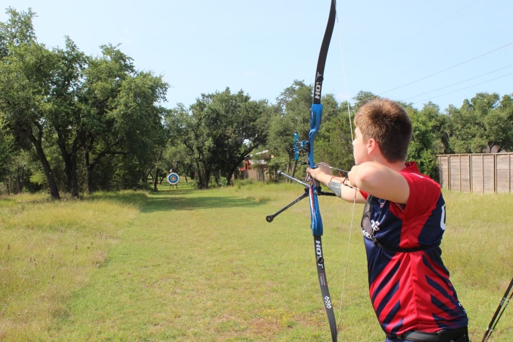 A teenage boy shoots a bow and arrow
