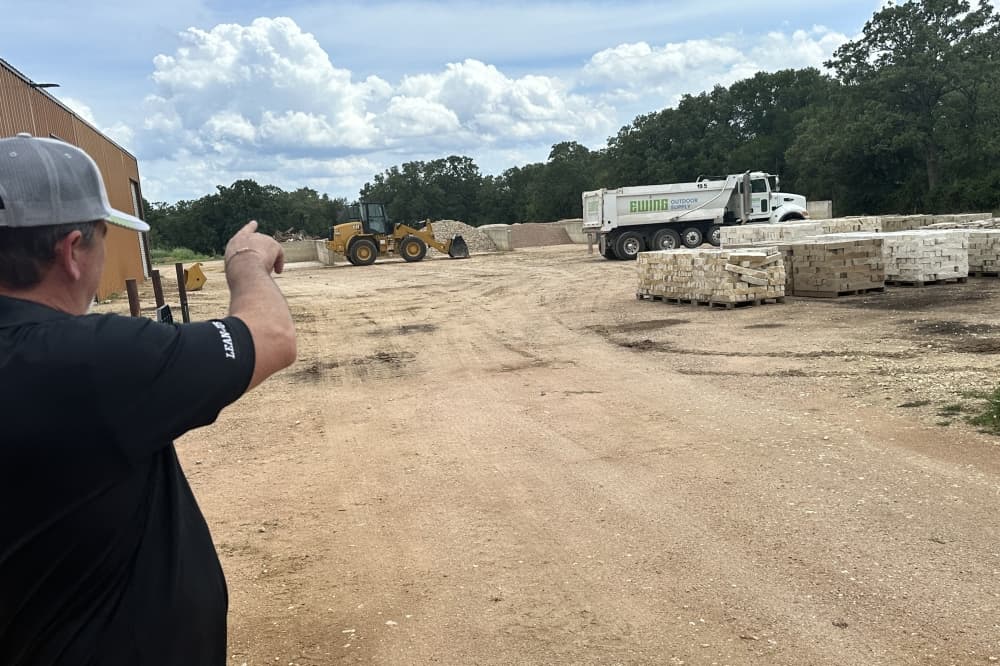 The manager points to trucks in the yard while explaining how deliveries work.