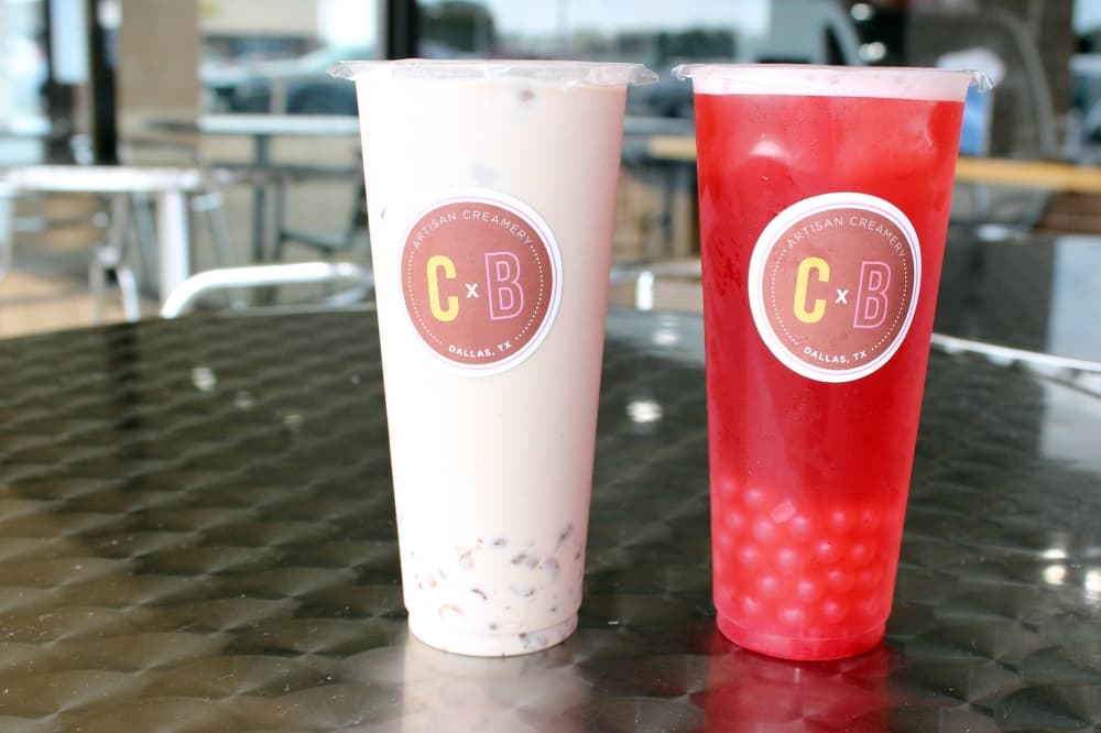 Two plastic cups filled with different colored liquid and boba. Cups have C&B logo stickers. 