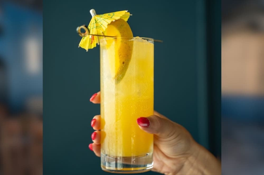 a person's hand holding a cocktail with a orange rind garnish and umbrella decoration