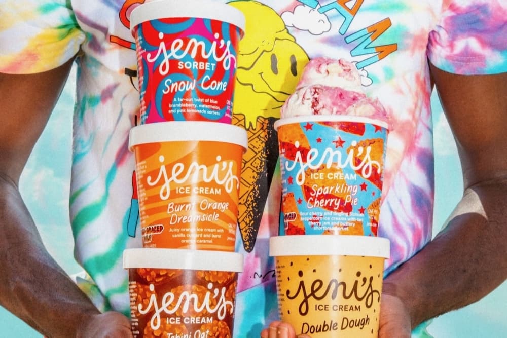 A person holding five different flavors of Jeni's Ice Cream (from left to right: Snow Cone sorbet, Burnt Orange Dreamsicle, Sparkling Cherry Pie, Tahini Oat Chocolate Chip and Double Dough).