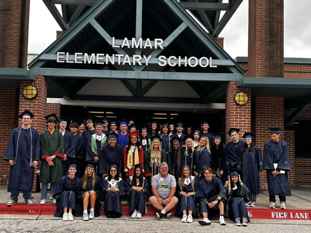 Students gather in front of a school in graduate gowns