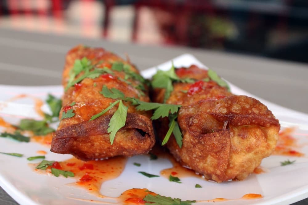Two egg rolls on a plate with orange liquid and greenery on top.