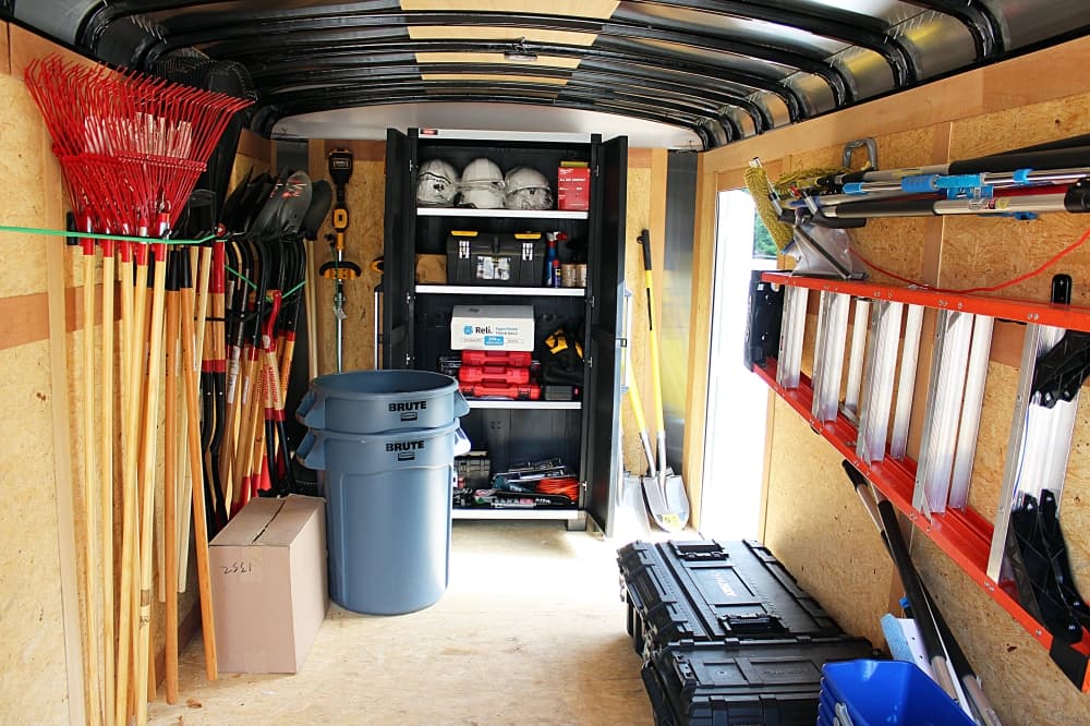 Tools, including rakes, ladders and shovels, hanging inside a trailer. 