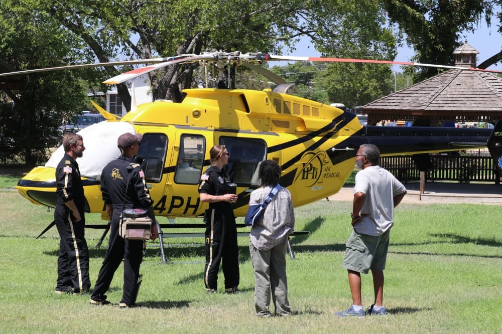 A medical helicopter is shown, with EMTs and attendees talking in front of it.