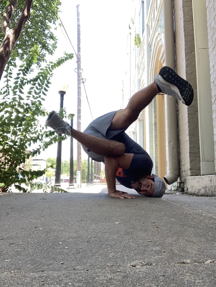 A man poses while break dancing outdoors on a sidewalk.
