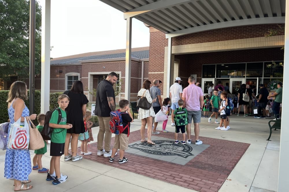 Students and parents greeted by staff entering school doors.