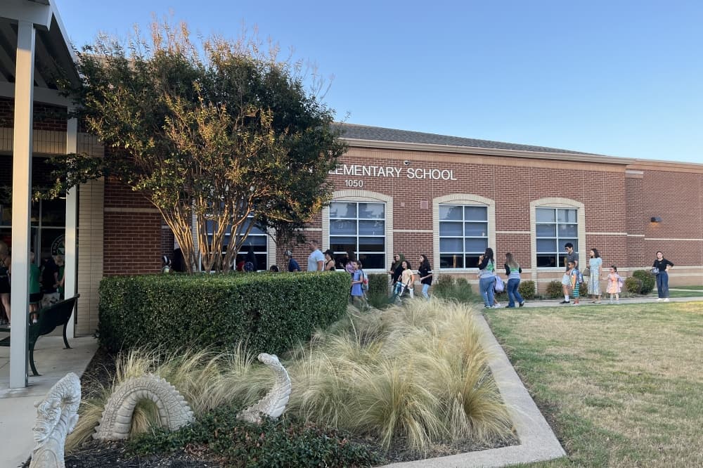 Students and parents greeted by staff entering school doors.