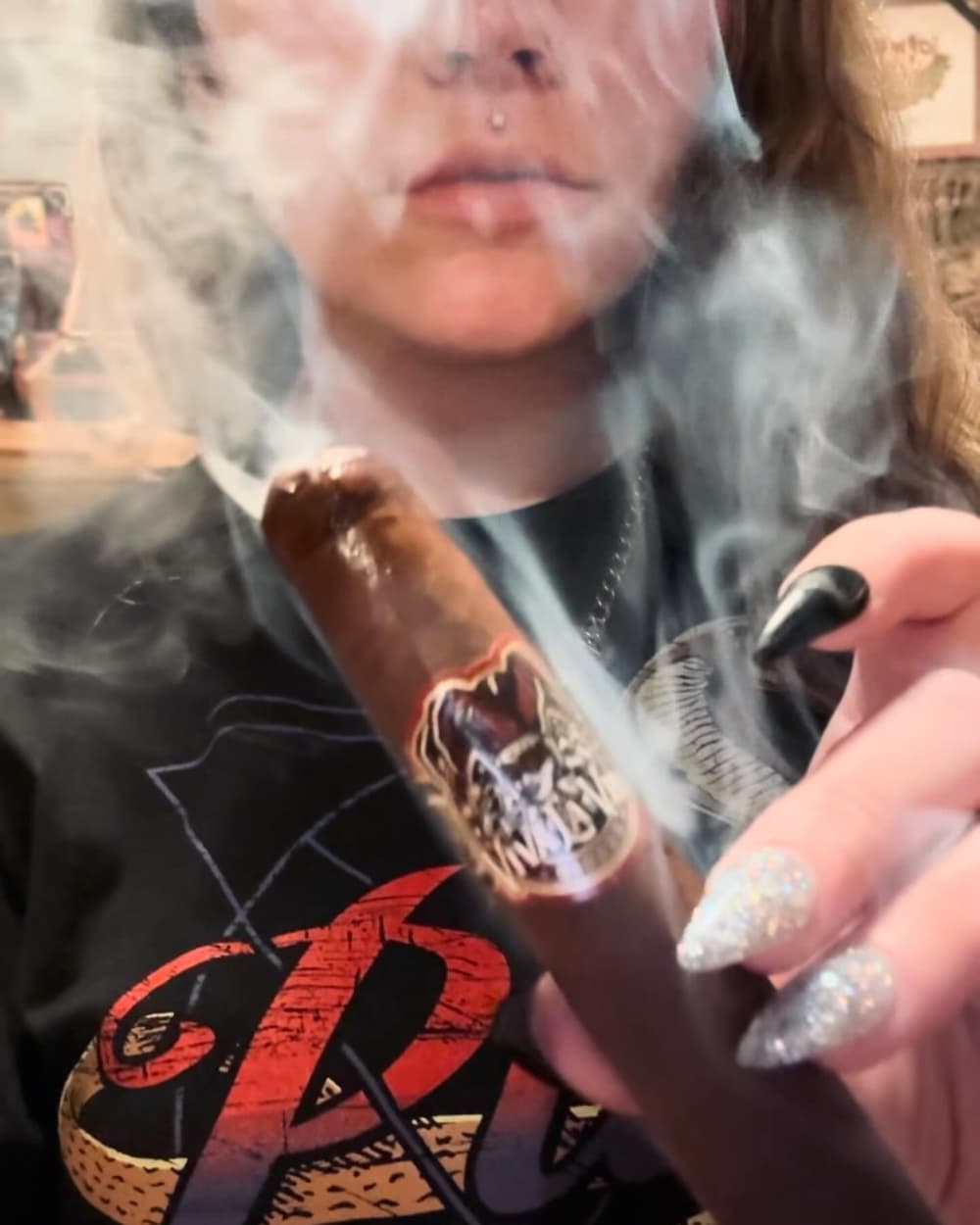 A woman holds up a cigar with smoke around her.