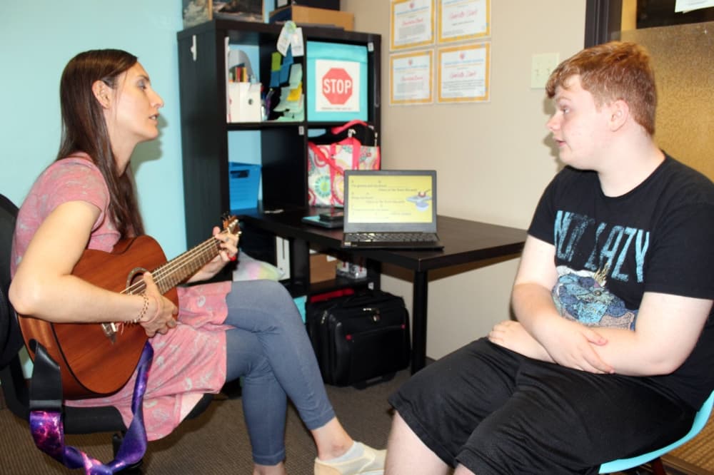 Female playing guitar while male watches. 