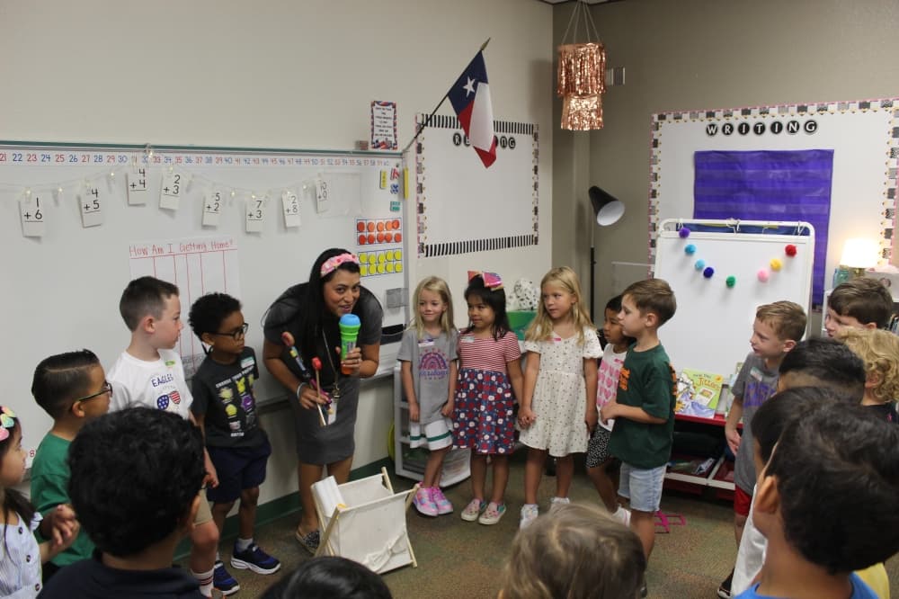First grade Teacher Jezzeka Sanchez holds up a toy microphone while her students are circled around her on the first day of school. 