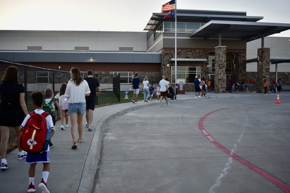 parents and students walk on a sidewalk toward an elementary school