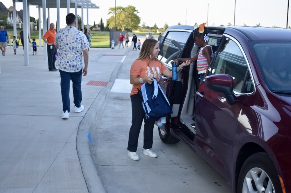 a principal helps a student out of a car