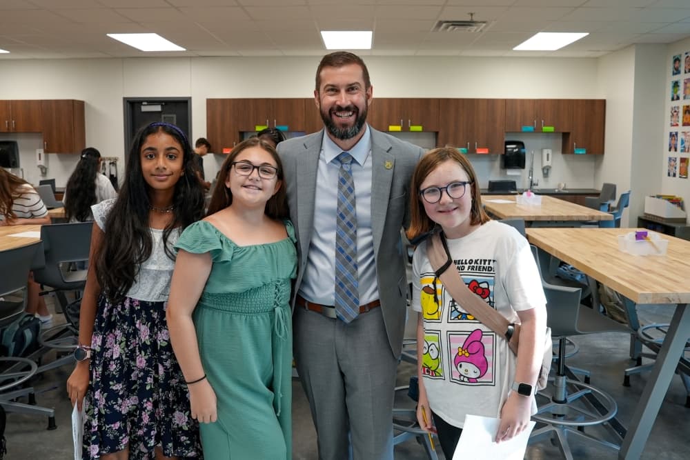 a principal of a middle school smiles with students