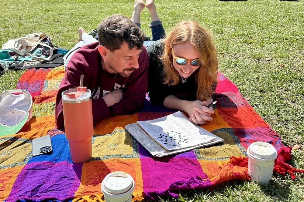 two people laying on blanket in a grassy field with books and cups