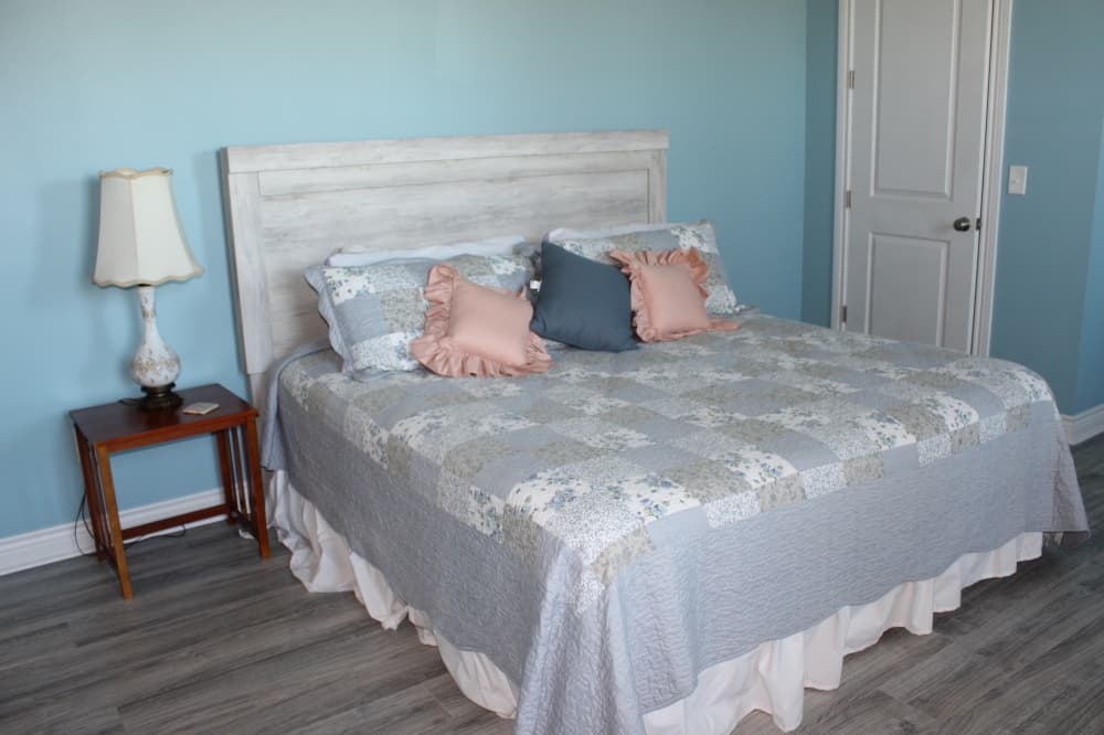 A bedroom with blue walls, a nightstand and a checkered quilt. 