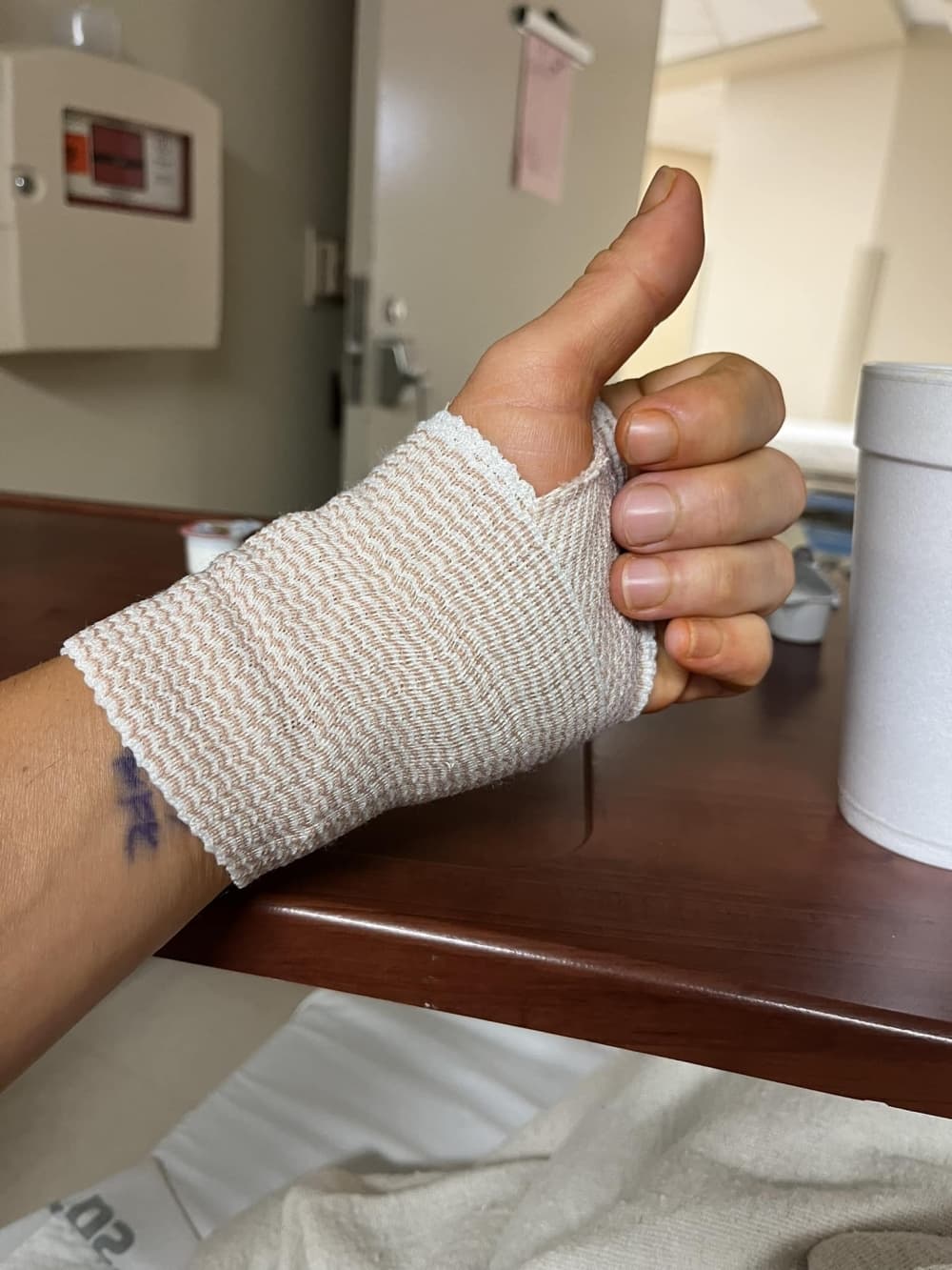 A bandaged hand gives a "thumbs up" sign.