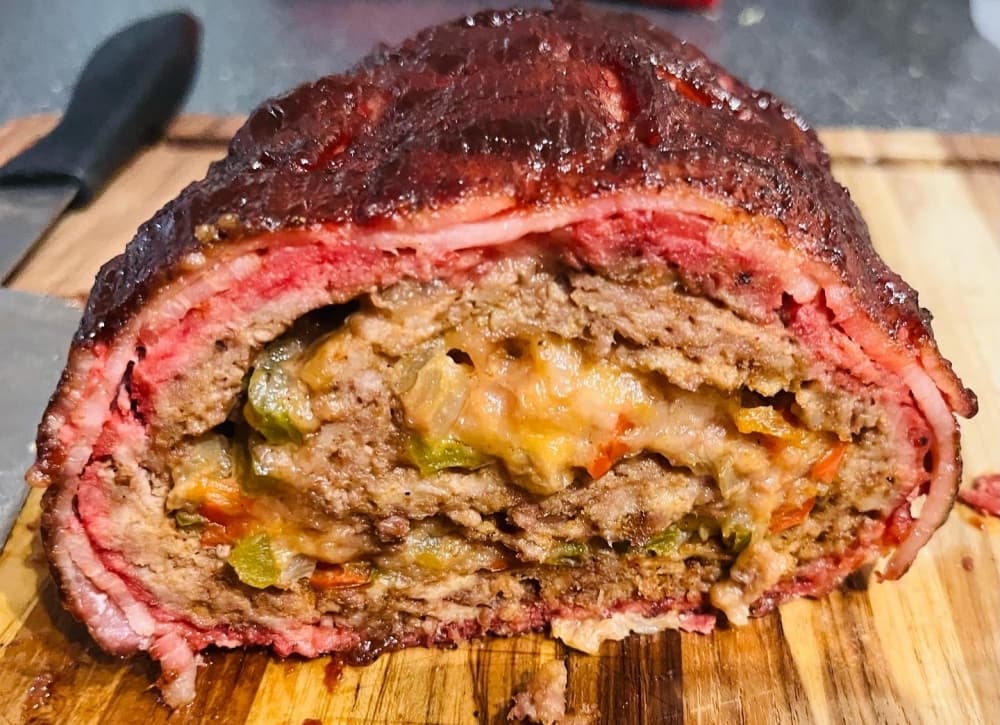 A meatloaf is shown cut in half, exposing laters of bacon, beef, cheese and more.