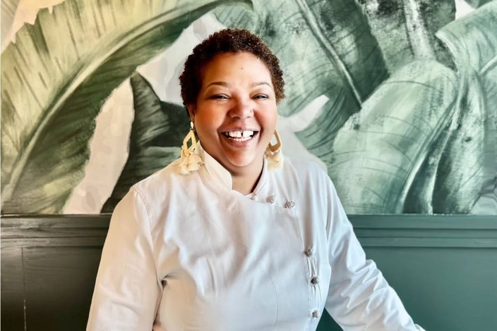 Female wearing chef's jacket in front of a wall with a plant mural.