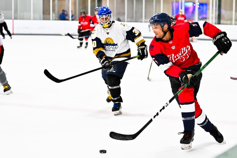 Two hockey participants skate towards the puck during a scrimmage. 