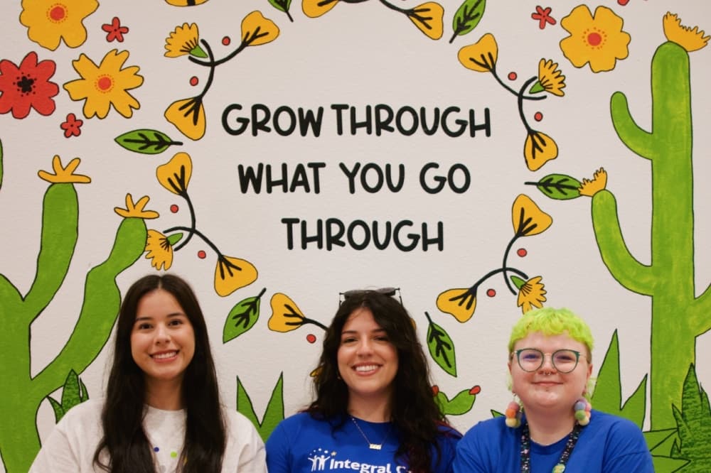providers pose in front of painting that reads "grow through what you go through"