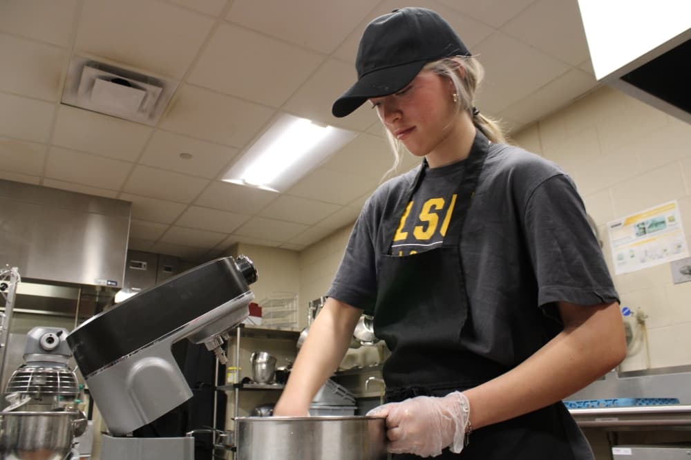 A high school student uses a mixer. 