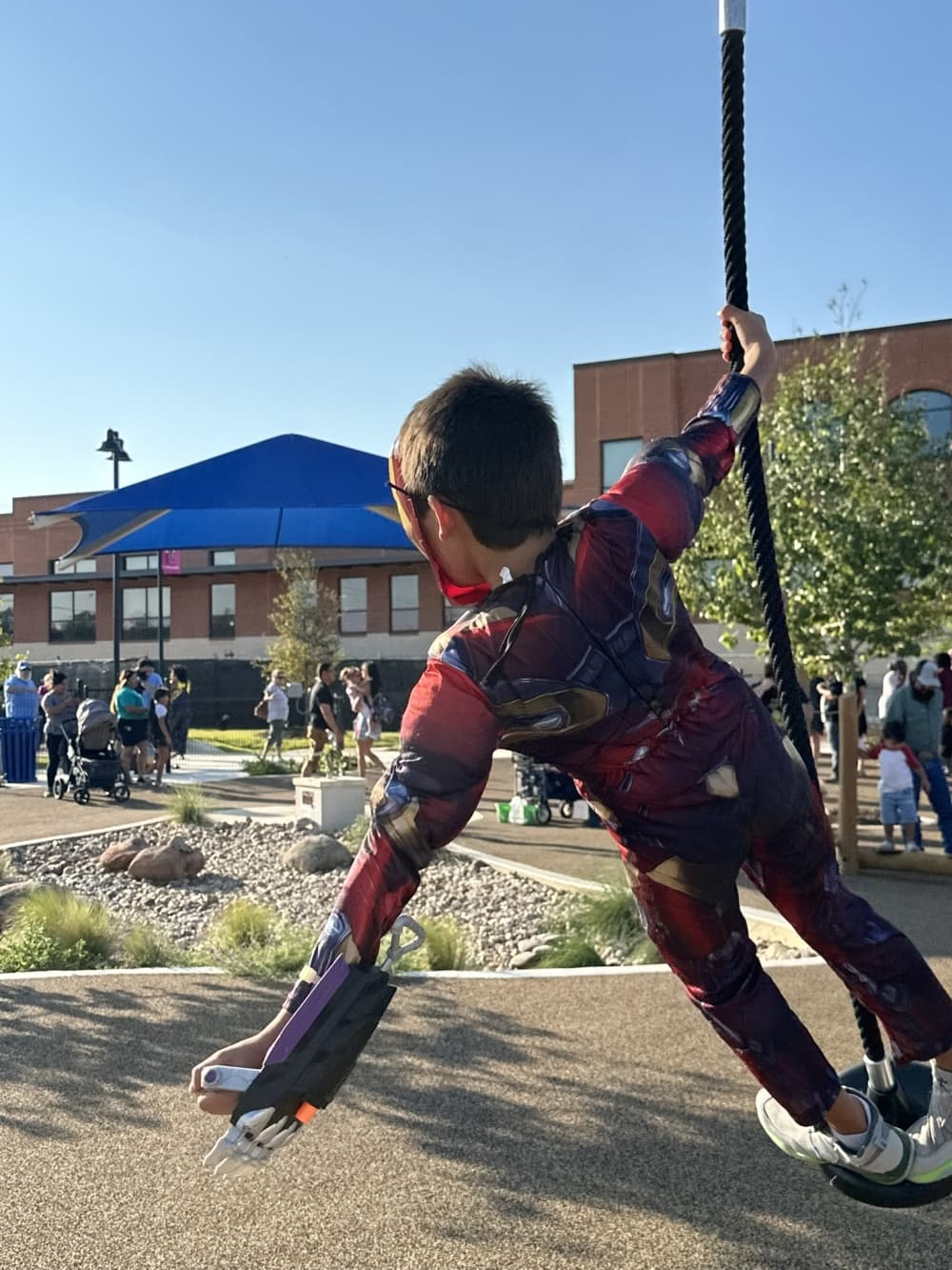 A child swings at the park dressed as Spiderman.