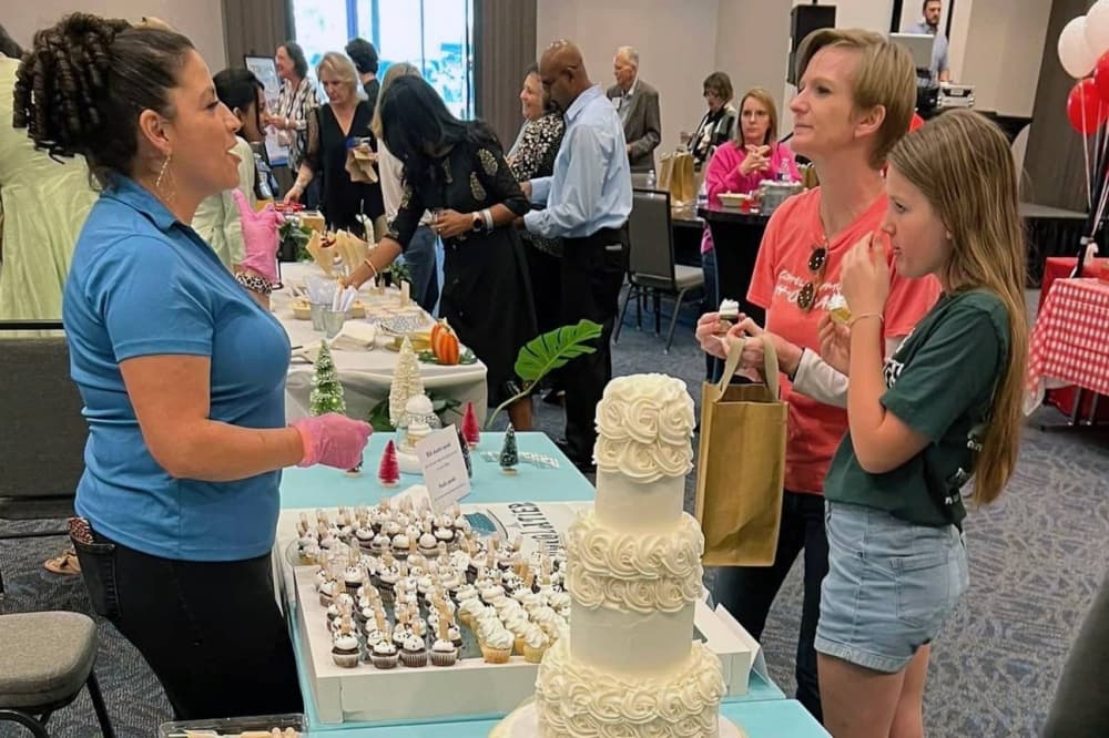 Three women gathered around a table with a large cake and slices of cake. 