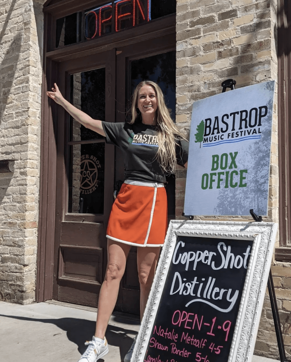 A woman poses in front of the box office at Copper Shot Distillery.