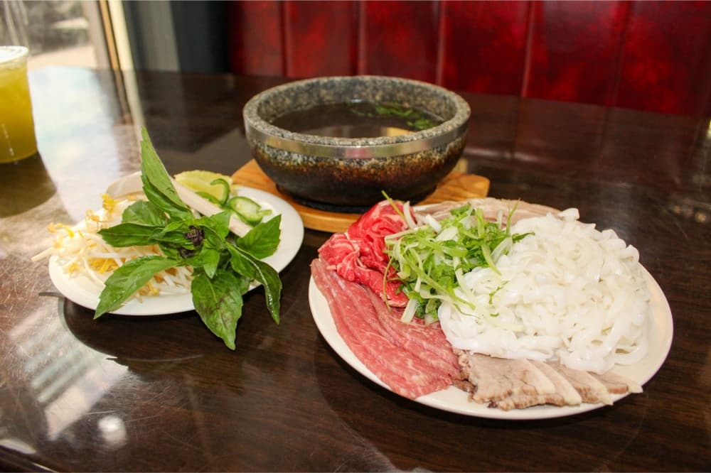 An image of the restaurant's stone bowl pho with the meat and vegetables on the side. 