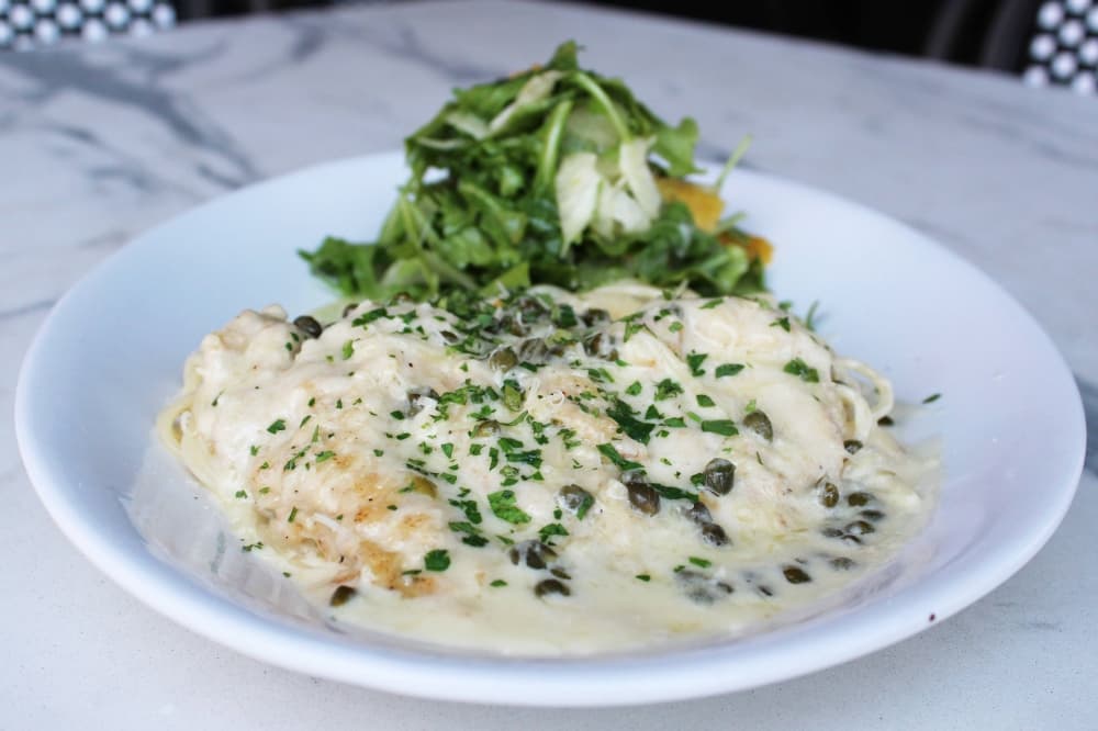 Bowl of pasta topped with white sauce, capers and arugula salad. 
