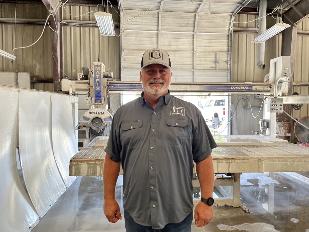 Man stands in front of a saw machine in an indoor shop. 