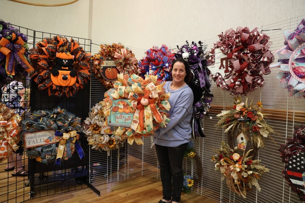 Female holding a wreath in front of multiple wreaths on display. 
