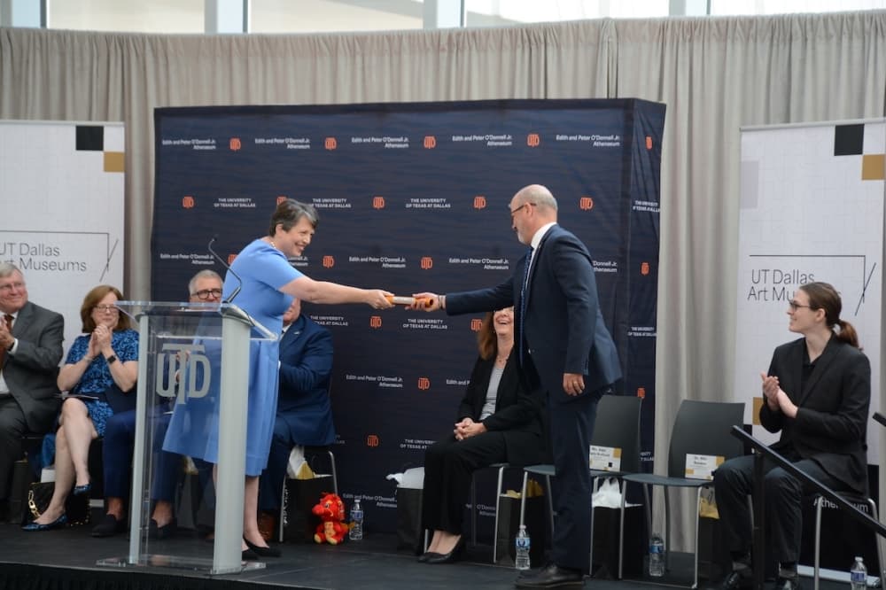 Crow Museum Executive Director Amy Lewis Hofland bestows a UT Dallas baton to Nils Roemer, dean of the Harry W. Bass Jr. School of the Arts, Humanities, and Technology at a ceremony Sept. 24. 