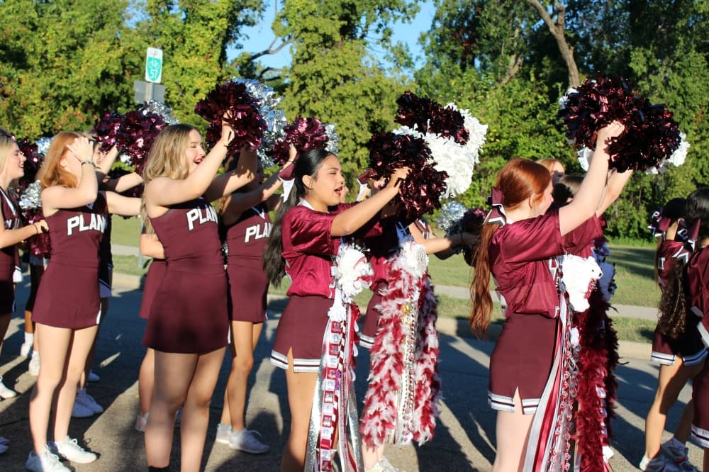 Cheerleaders wearing maroon and white uniforms raising pompoms.