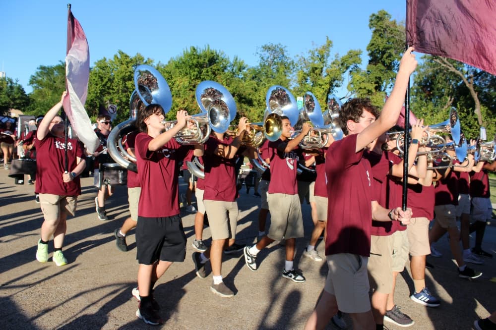 Band members wearing maroon shirts marching in a parade.