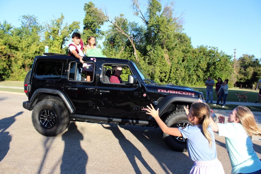 Teens in a jeep tossing candy to children.